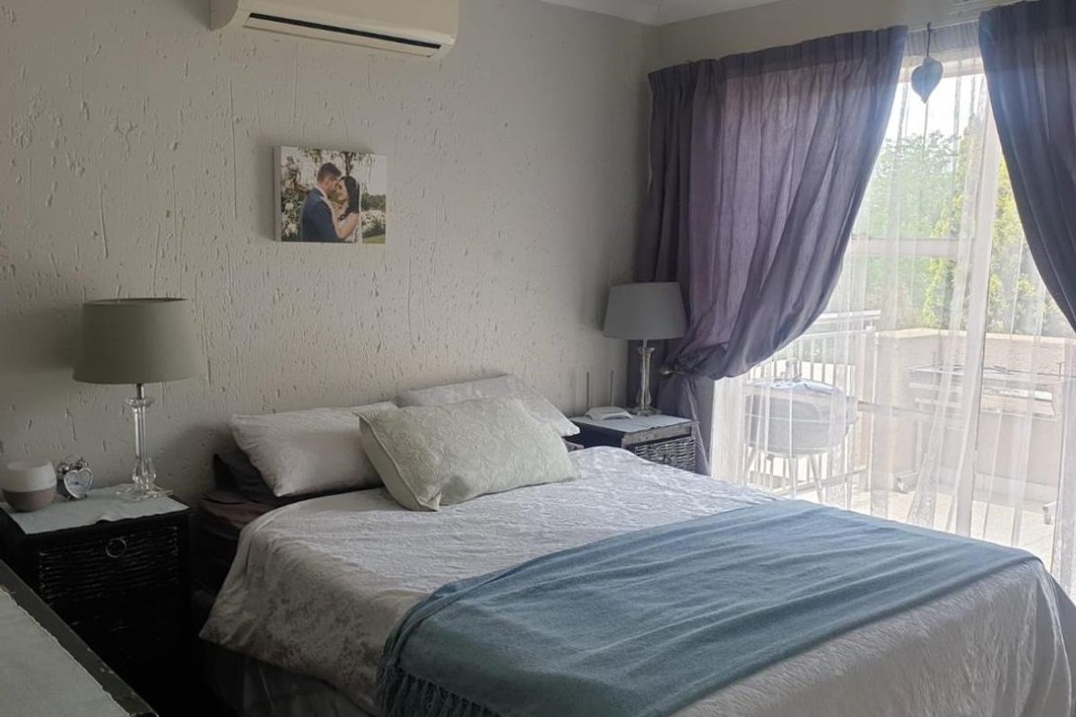 A bedroom featuring a split-system air conditioner, textured walls, and a sliding glass door providing access to an outdoor balcony area.