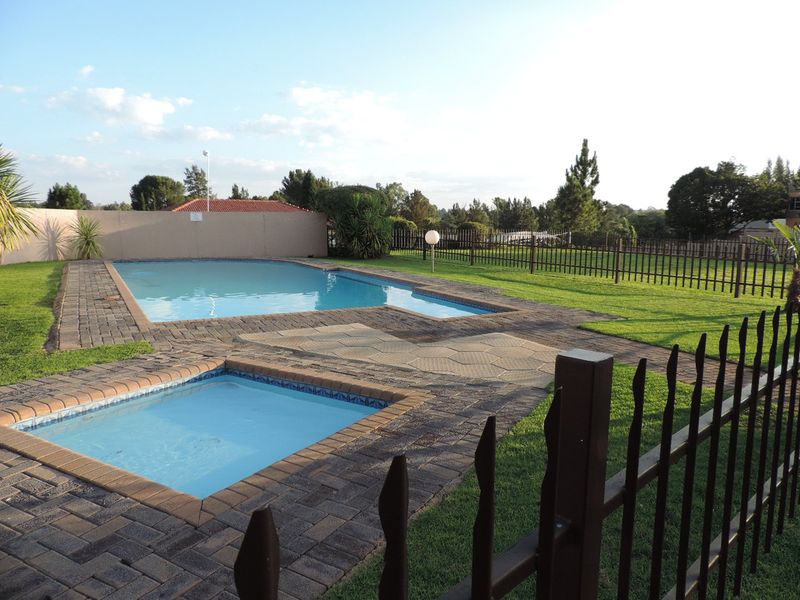 A well-maintained communal pool area featuring a swimming pool, a smaller spa pool, paved surrounds, and secure metal perimeter fencing.