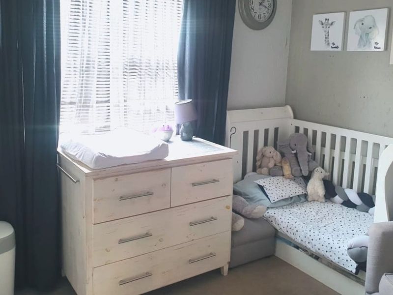 A bedroom featuring neutral wall tones and venetian blinds, providing a functional space for a nursery or child's room.