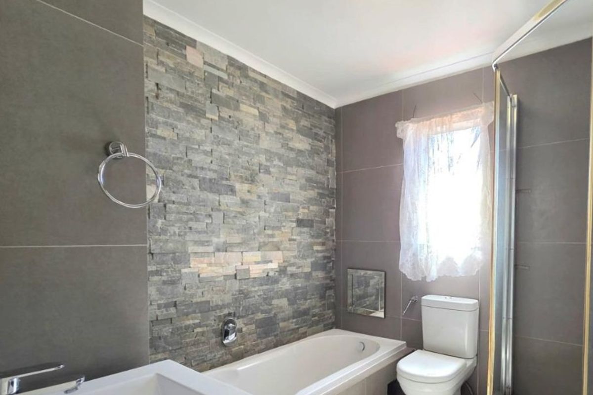 Modern bathroom featuring a stone feature wall, built-in bathtub, separate shower enclosure, and a vanity basin with neutral tiled finishes.