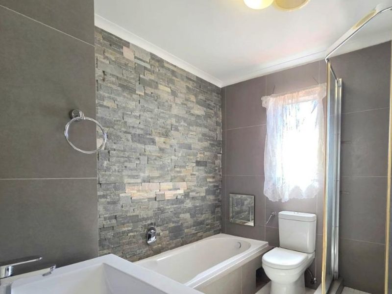 Modern bathroom featuring a stone feature wall, built-in bathtub, separate shower enclosure, and a vanity basin with neutral tiled finishes.