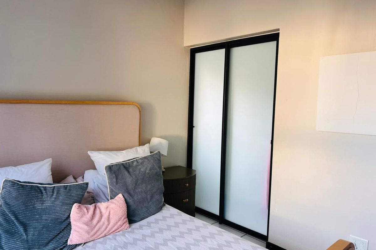 A bedroom featuring a built-in wardrobe with black-framed frosted glass sliding doors and neutral wall finishes.