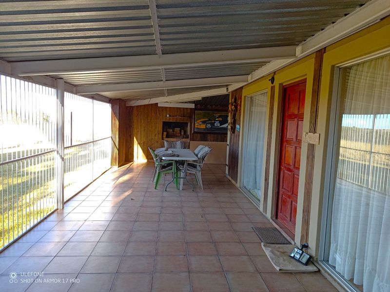 A covered outdoor patio featuring tiled flooring, timber wall cladding, and a built-in braai area, providing a functional space for outdoor entertaining.