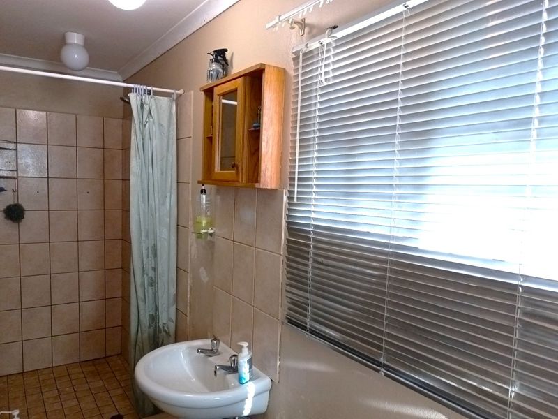 A functional bathroom featuring a shower area, wall-mounted basin, and tiled finishes, requiring some cosmetic updates to improve its overall condition.