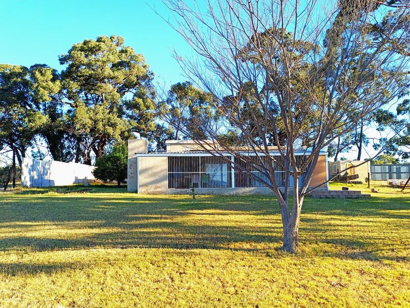 Rear view of the farm dwelling featuring a concrete patio, security bars on windows, and a masonry chimney set within a large garden.