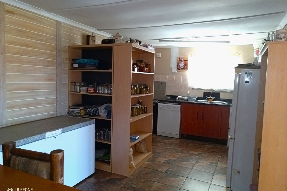 A functional kitchen area featuring tiled flooring, timber wall paneling, and basic cabinetry with a stainless steel sink and tiled backsplash.