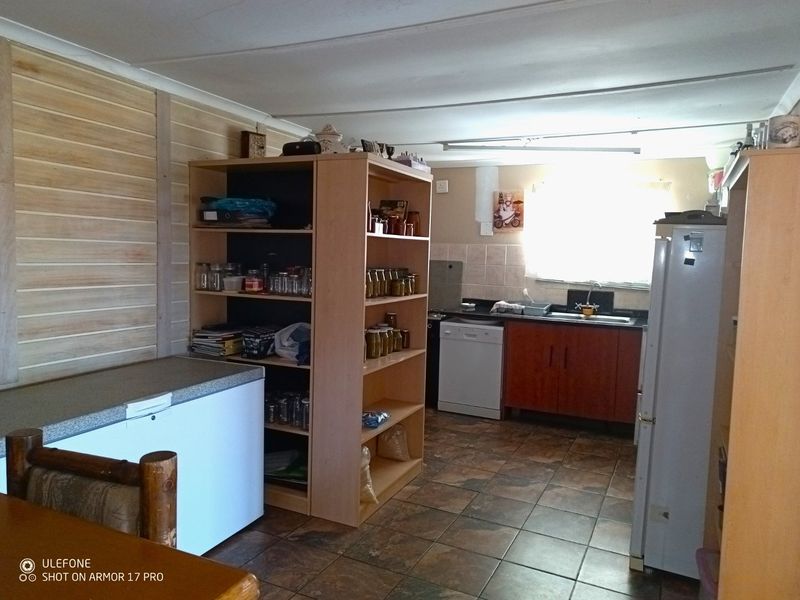 A functional kitchen area featuring tiled flooring, timber wall paneling, and basic cabinetry with a stainless steel sink and tiled backsplash.