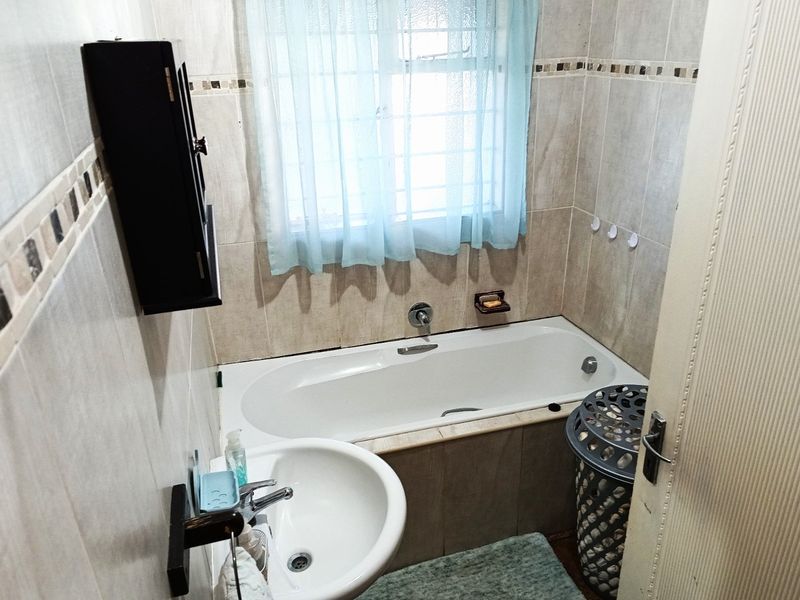 A functional bathroom featuring a built-in bathtub, pedestal washbasin, and neutral wall tiling with decorative accents.