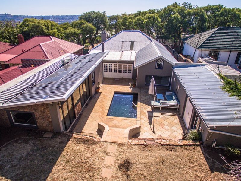 Aerial view of the property featuring a central swimming pool, paved patio area, and a house with solar panels and corrugated metal roofing.