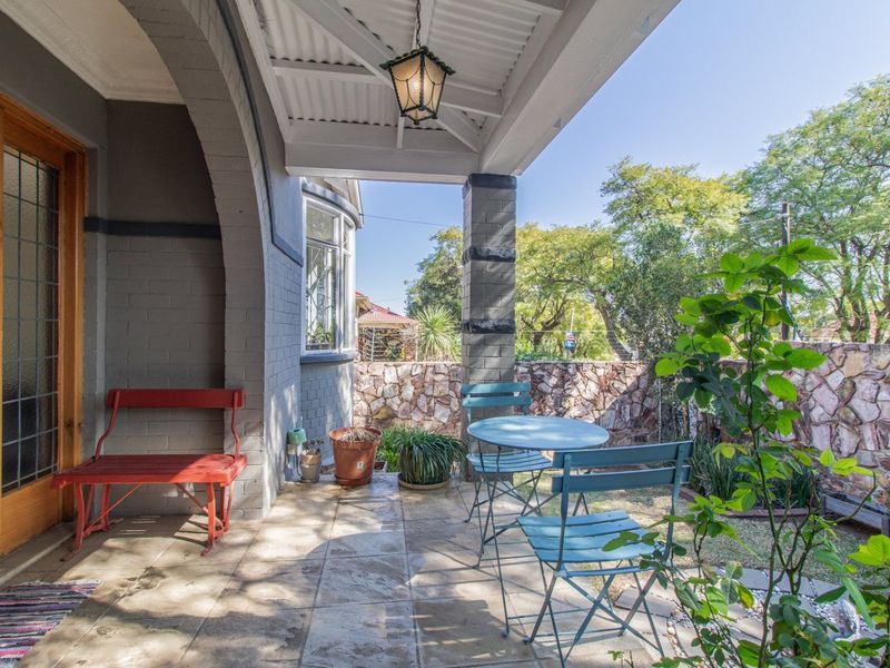 A covered patio area featuring tiled flooring, an arched masonry pillar, and a stone boundary wall, providing a pleasant outdoor seating space.