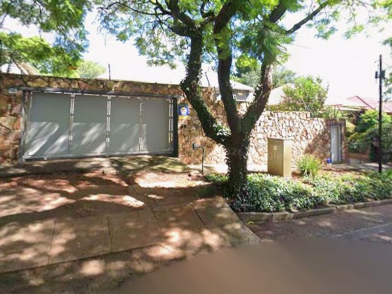 Front view of the property featuring a stone-clad boundary wall, secure sliding gate, electric fencing, and a paved driveway entrance.