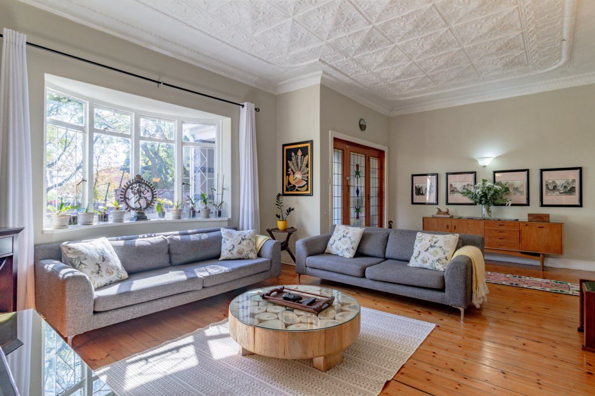 Spacious living room featuring original timber flooring, a decorative pressed metal ceiling, and a large bay window that provides ample natural light.