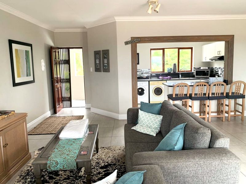 An open-plan living area featuring tiled floors, a breakfast bar, and a functional kitchen with built-in cabinetry and an extractor fan.