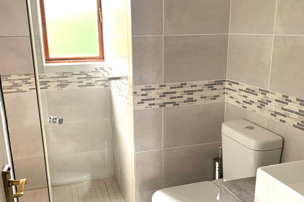 Modern bathroom featuring a walk-in shower with glass screen, a concrete vanity with vessel sink, and neutral wall tiling with a decorative mosaic border.