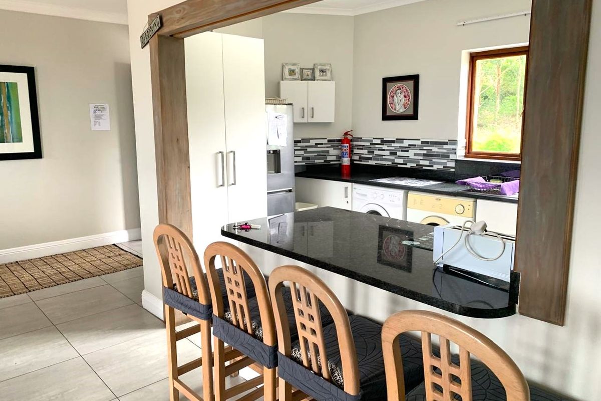 A functional kitchen featuring a granite breakfast bar, tiled splashback, and integrated laundry appliances, viewed through a timber-framed opening from the living area.