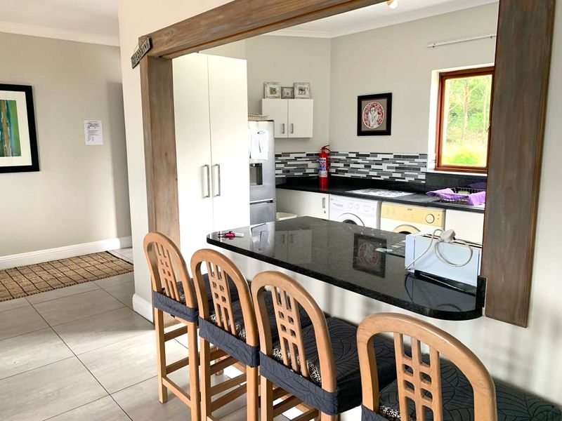 A functional kitchen featuring a granite breakfast bar, tiled splashback, and integrated laundry appliances, viewed through a timber-framed opening from the living area.
