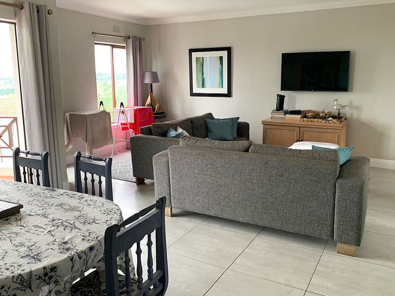 Spacious open-plan living and dining area featuring neutral tiled flooring, coving, and direct access to an outdoor balcony through sliding glass doors.