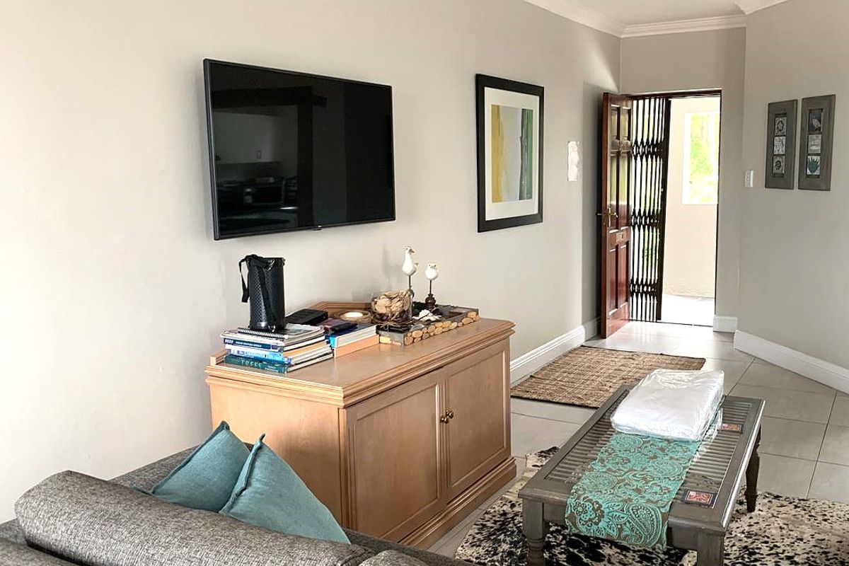 A well-maintained living room featuring tiled flooring, decorative coving, and a secure entrance door with a fitted security gate.