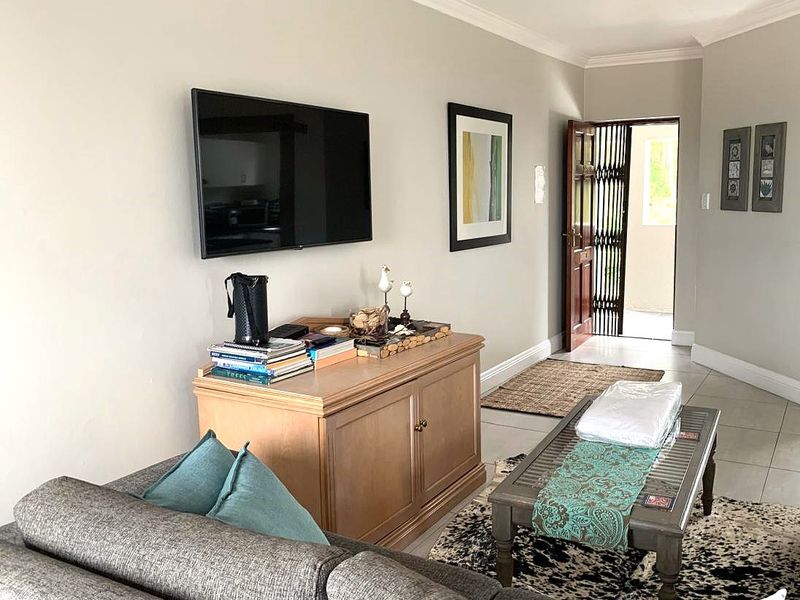 A well-maintained living room featuring tiled flooring, decorative coving, and a secure entrance door with a fitted security gate.