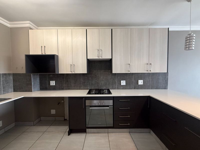 Modern kitchen featuring two-tone cabinetry, stone countertops, built-in gas hob, and oven with a tiled backsplash and neutral floor tiles.
