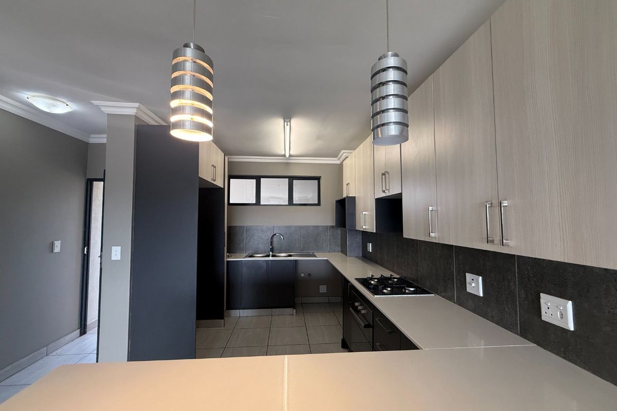 Modern kitchen featuring sleek two-tone cabinetry, stone countertops, a gas hob, built-in oven, and contemporary pendant lighting in an open-plan layout.