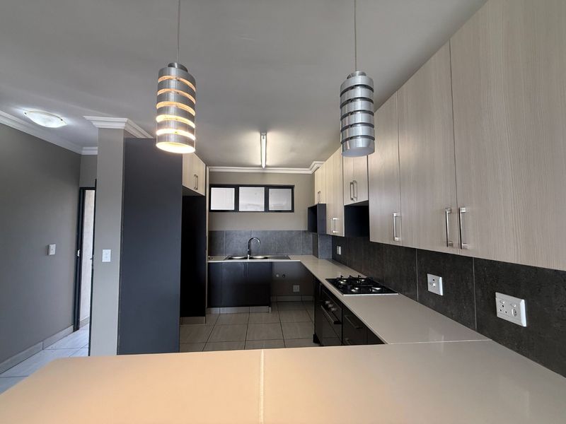 Modern kitchen featuring sleek two-tone cabinetry, stone countertops, a gas hob, built-in oven, and contemporary pendant lighting in an open-plan layout.
