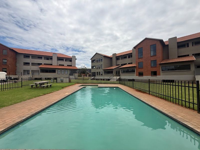 Communal swimming pool area featuring paved surrounds and metal perimeter fencing, set within a well-maintained apartment complex courtyard.