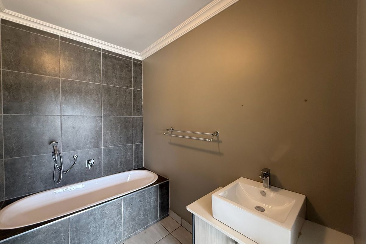 A functional bathroom featuring a built-in bathtub with grey tiling, a modern vessel sink vanity, and crown molding detail.