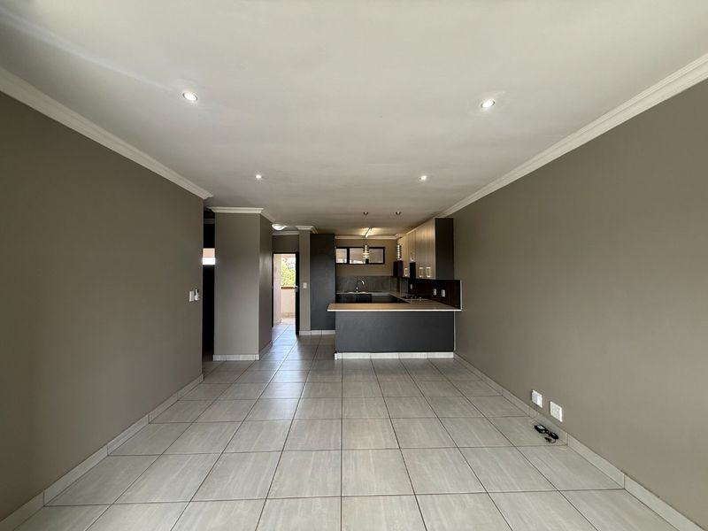 Spacious open-plan living and kitchen area featuring neutral wall tones, ceramic tiled flooring, recessed lighting, and modern kitchen cabinetry with a breakfast bar.