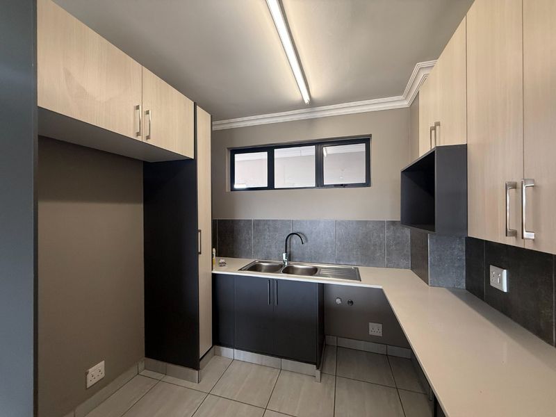 A clean, modern kitchen featuring light wood and dark cabinetry, stone countertops, a double bowl sink, and tiled flooring.