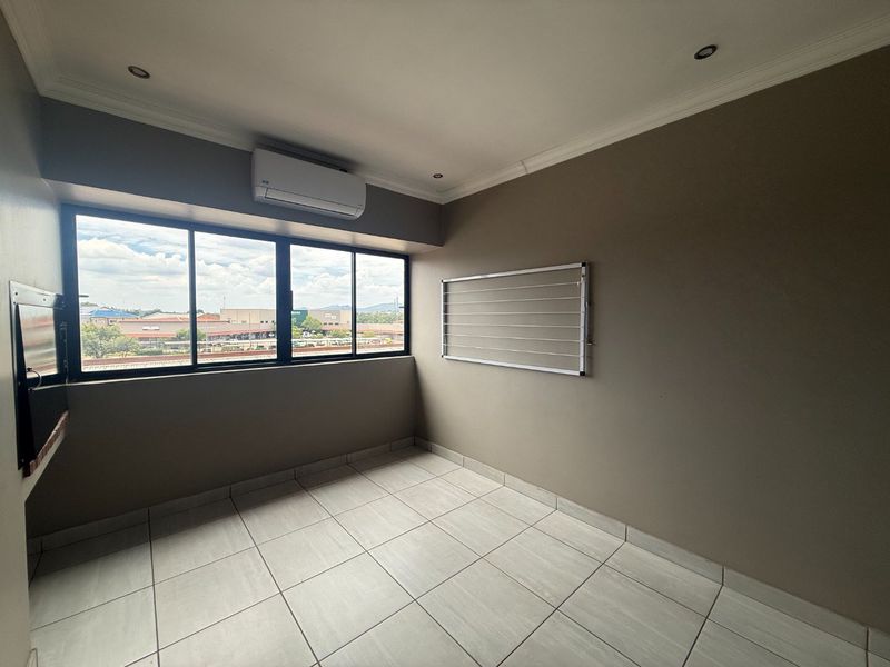 A clean, empty utility space featuring tiled flooring, recessed lighting, an air conditioning unit, and a wall-mounted drying rack with large windows.
