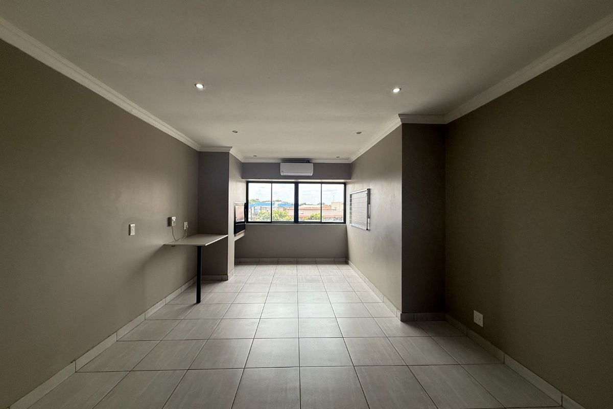 A spacious, empty living area featuring neutral tiled floors, recessed lighting, a wall-mounted air conditioning unit, and a convenient built-in desk space.
