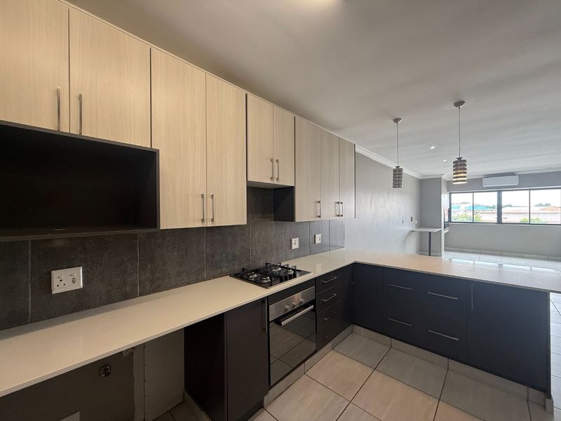 Modern open-plan kitchen featuring two-tone cabinetry, stone countertops, built-in gas hob and oven, flowing into a spacious living area with tiled floors.