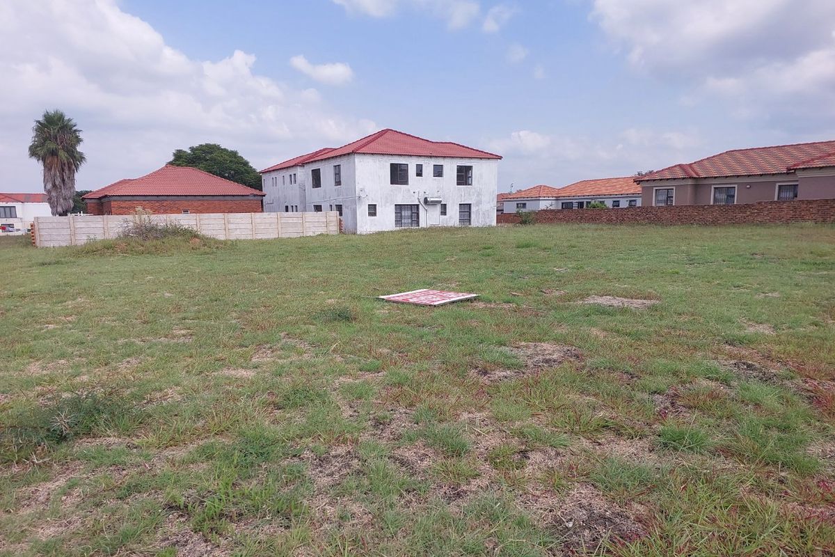 A vacant residential plot featuring a grass lawn, enclosed by perimeter walls, situated in a developed neighborhood setting.