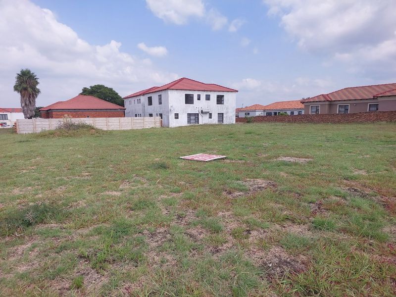 A vacant residential plot featuring a grass lawn, enclosed by perimeter walls, situated in a developed neighborhood setting.