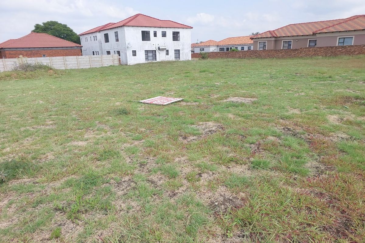 A vacant residential plot featuring a grass lawn and perimeter walling, situated in a developed neighborhood.