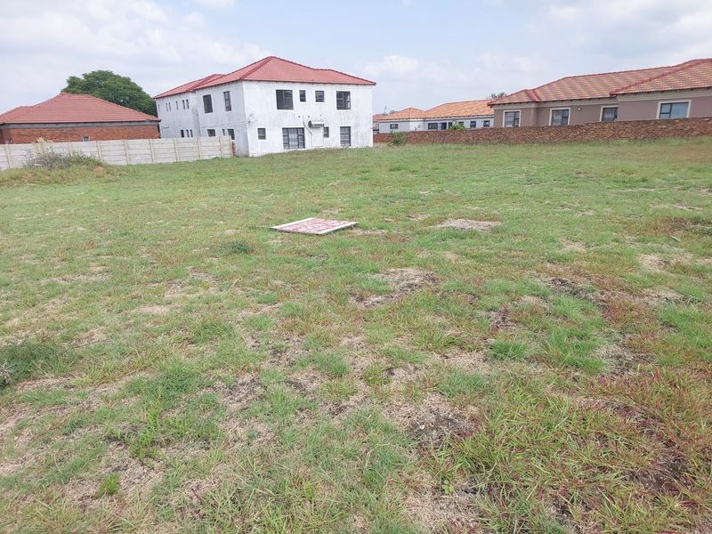 A vacant residential plot featuring a grass lawn and perimeter walling, situated in a developed neighborhood.