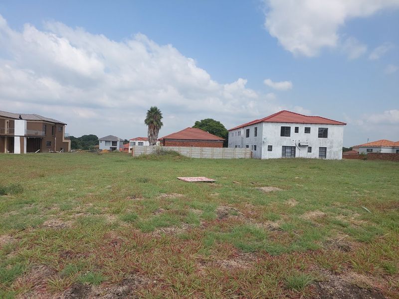 A vacant residential plot of land featuring a grass lawn and a precast concrete boundary wall, situated in a developed neighborhood.
