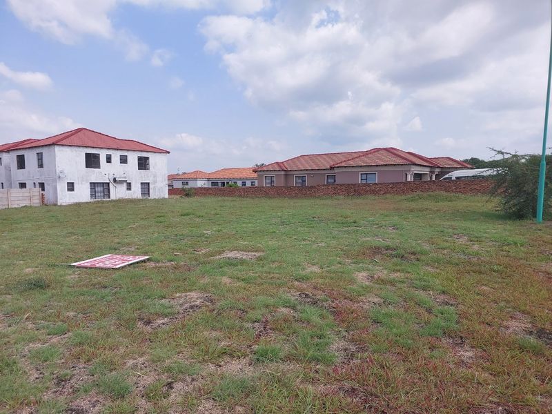 A vacant residential plot of land featuring a grass lawn and a brick boundary wall, situated in a developed neighborhood.