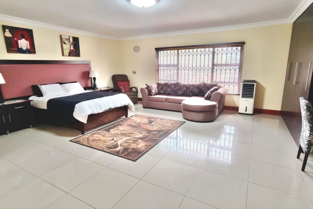 Spacious bedroom featuring large built-in cupboards, tiled flooring, and a window fitted with security bars.