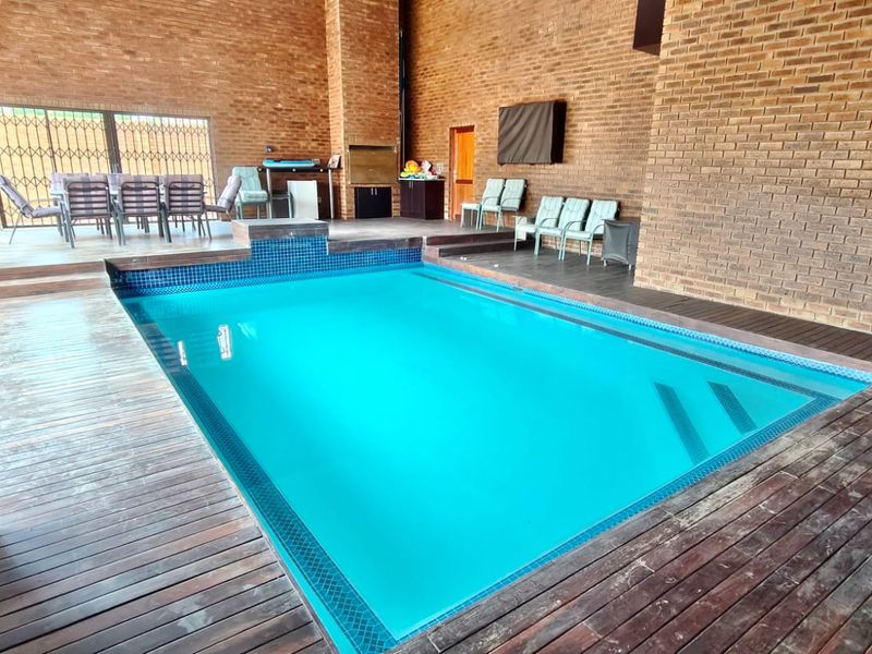 Spacious indoor pool area featuring exposed brick walls, timber decking, and a built-in braai, perfect for year-round entertainment.