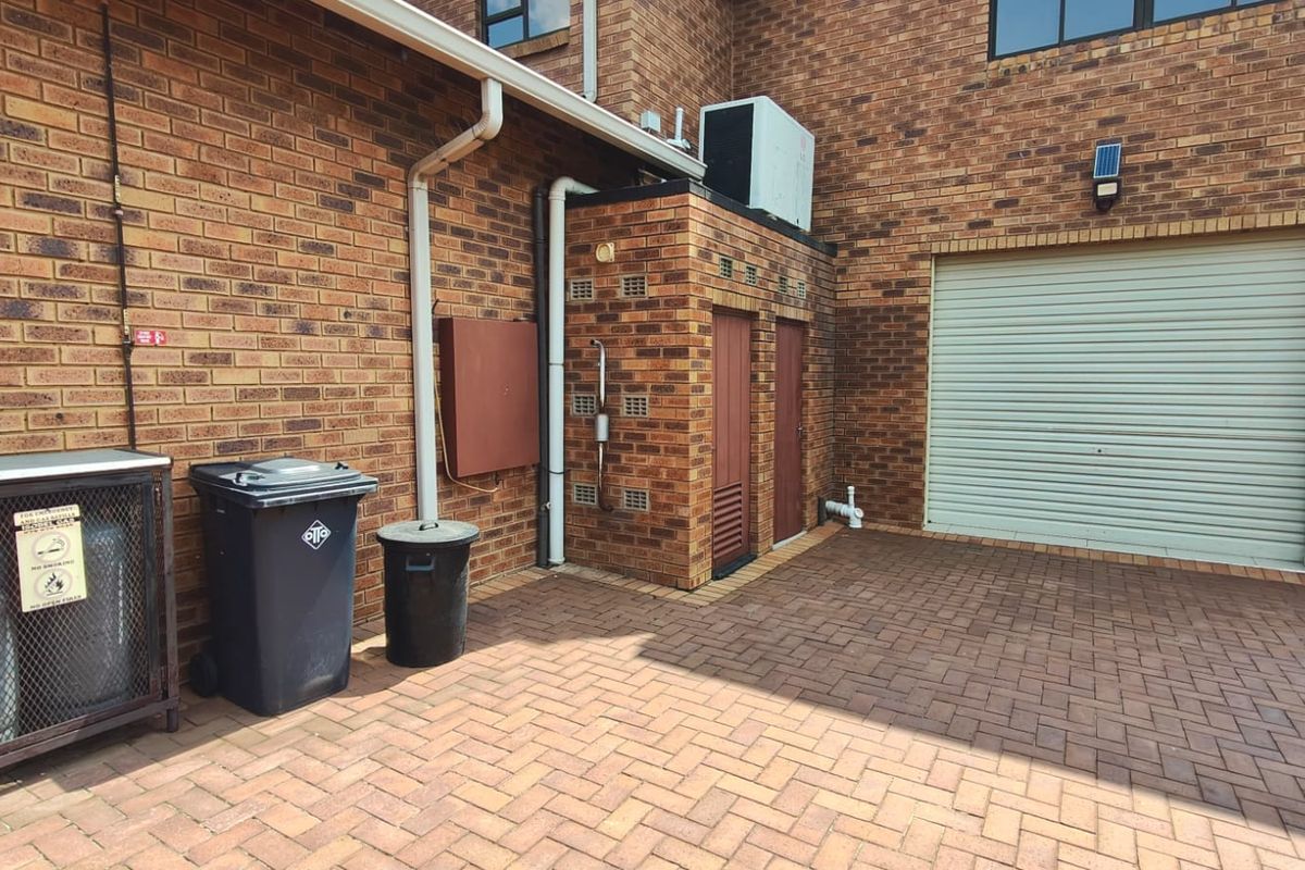A paved rear courtyard area featuring brick wall construction, a roller garage door, and integrated exterior utility fixtures.