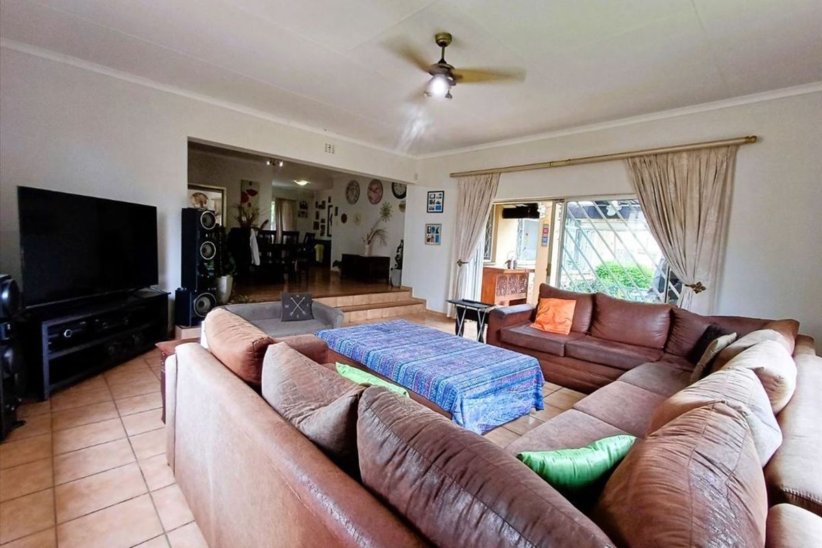 Spacious open-plan living area featuring tiled floors, a ceiling fan, and a raised transition to the adjacent dining space with sliding door access.