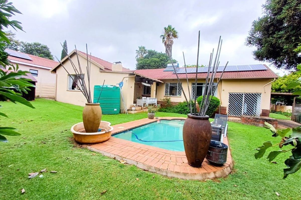 Rear view of the property featuring a swimming pool, brick paved surround, solar panels on the roof, and a large water storage tank.