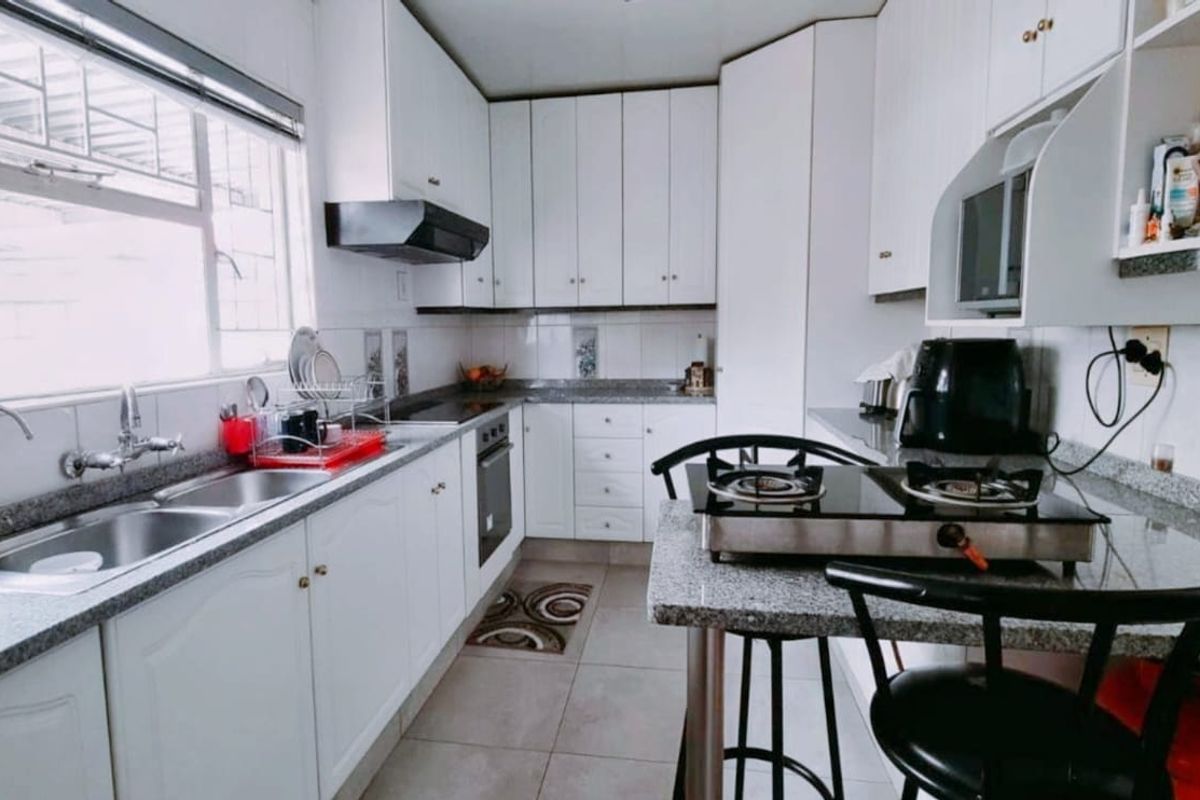 A functional kitchen featuring white cabinetry, granite countertops, a double basin sink, built-in oven, and an extractor fan with tiled flooring and backsplash.