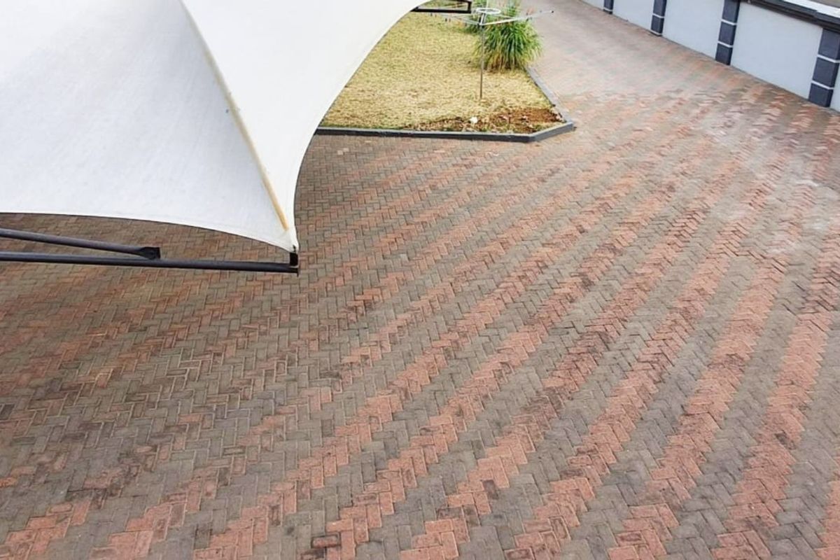A paved rear courtyard area featuring a large shade sail, perimeter boundary wall, and a small landscaped garden section.