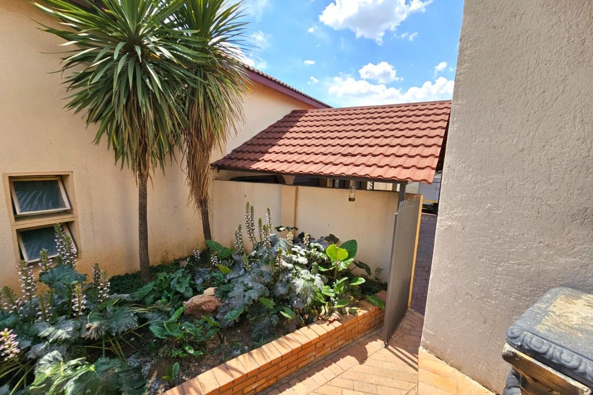 A well-maintained rear garden area featuring a brick-paved walkway, a raised brick planter bed, and a covered side access path with a tiled roof.