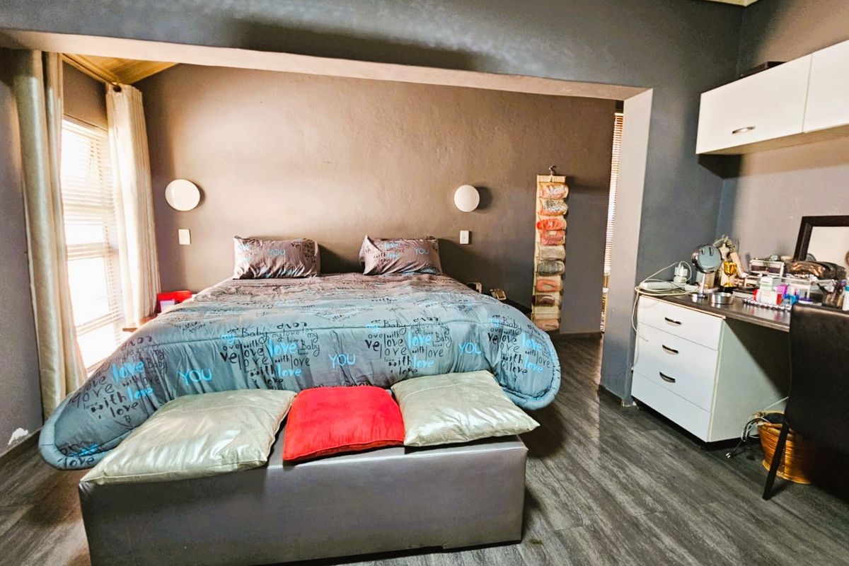 A bedroom featuring dark grey walls, laminate flooring, and a built-in desk area with overhead storage cabinetry.