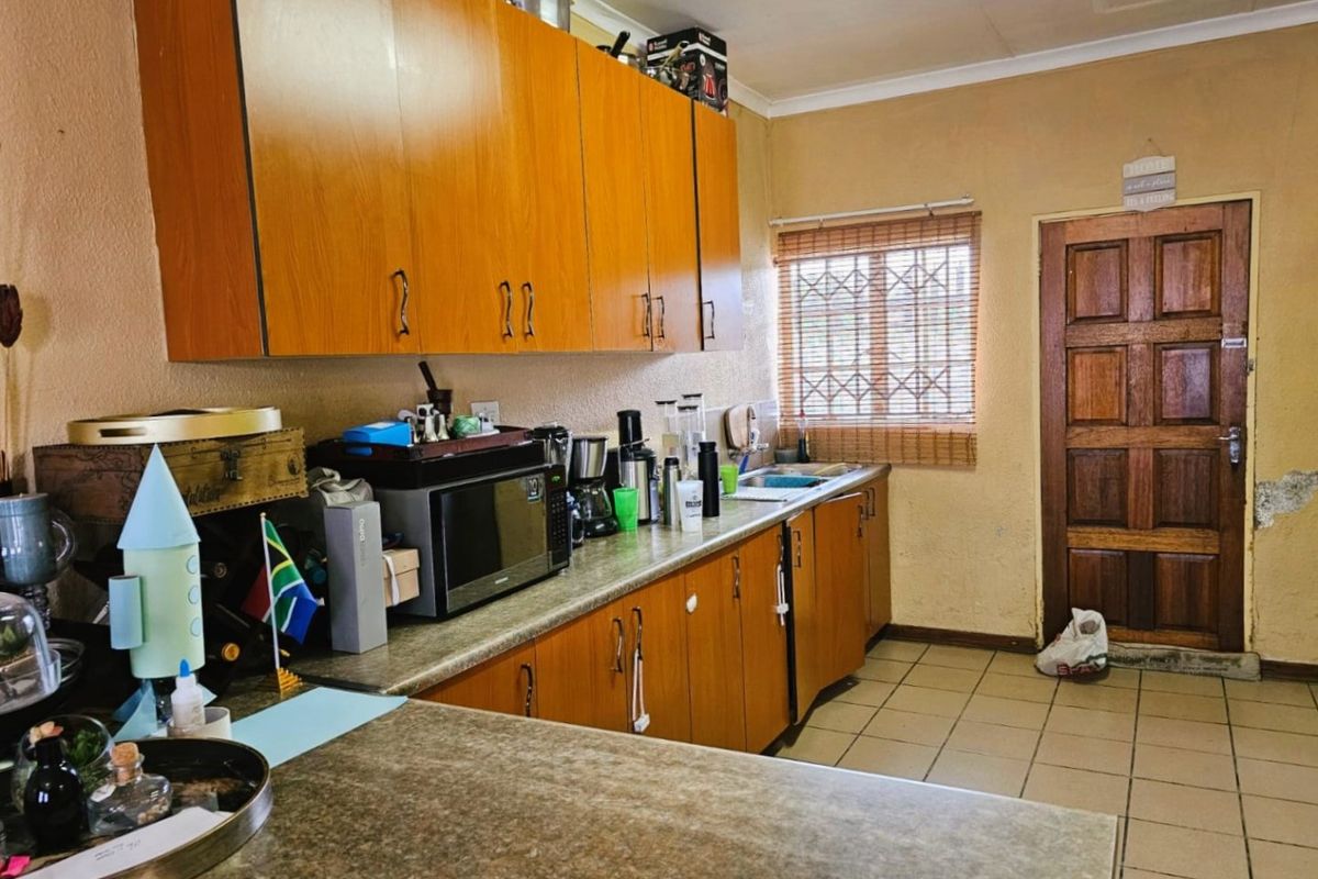 A functional kitchen featuring wood-look cabinetry, laminate countertops, tiled flooring, and a security gate on the window.