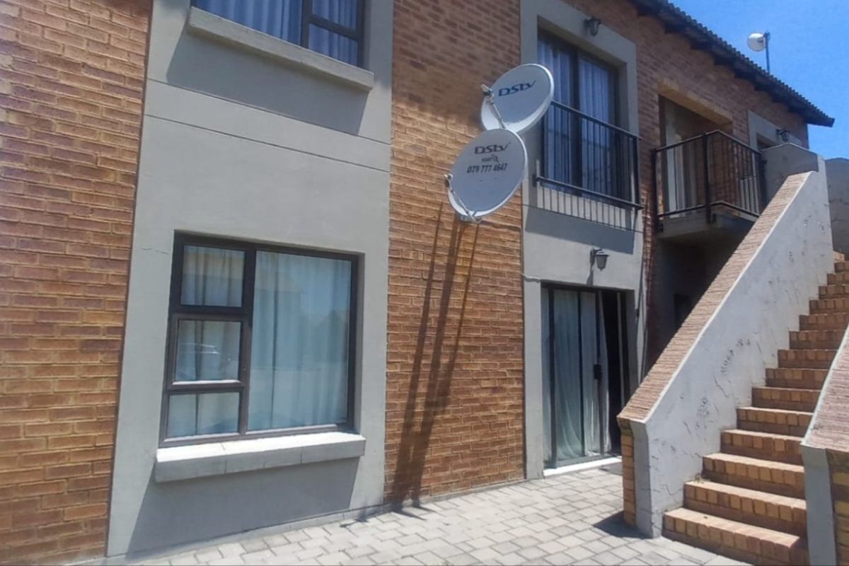 Rear view of a brick apartment building featuring an external staircase, paved patio area, and balcony access.